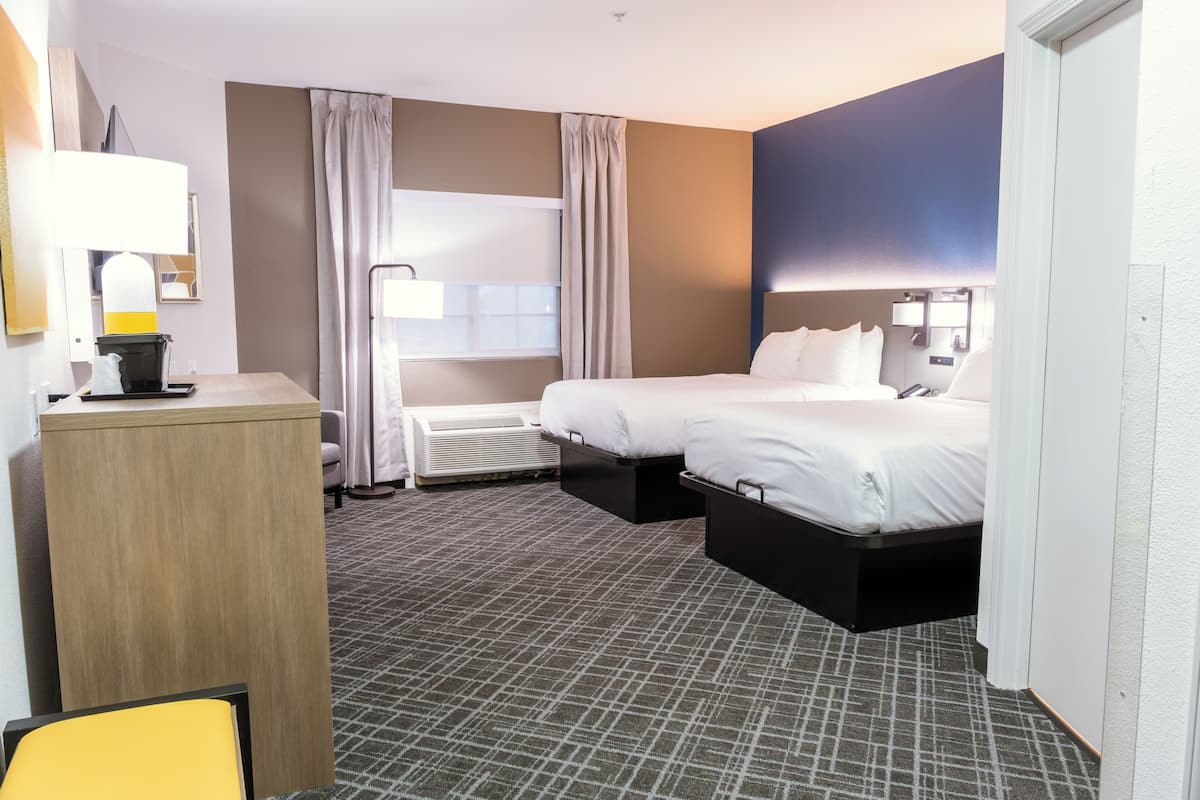 A hotel room with a bed, bedside table, lamp, and a window with curtains.