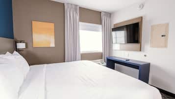 A hotel room with a large bed, a desk, a flat-screen TV, a window with curtains, and a wall-mounted artwork.