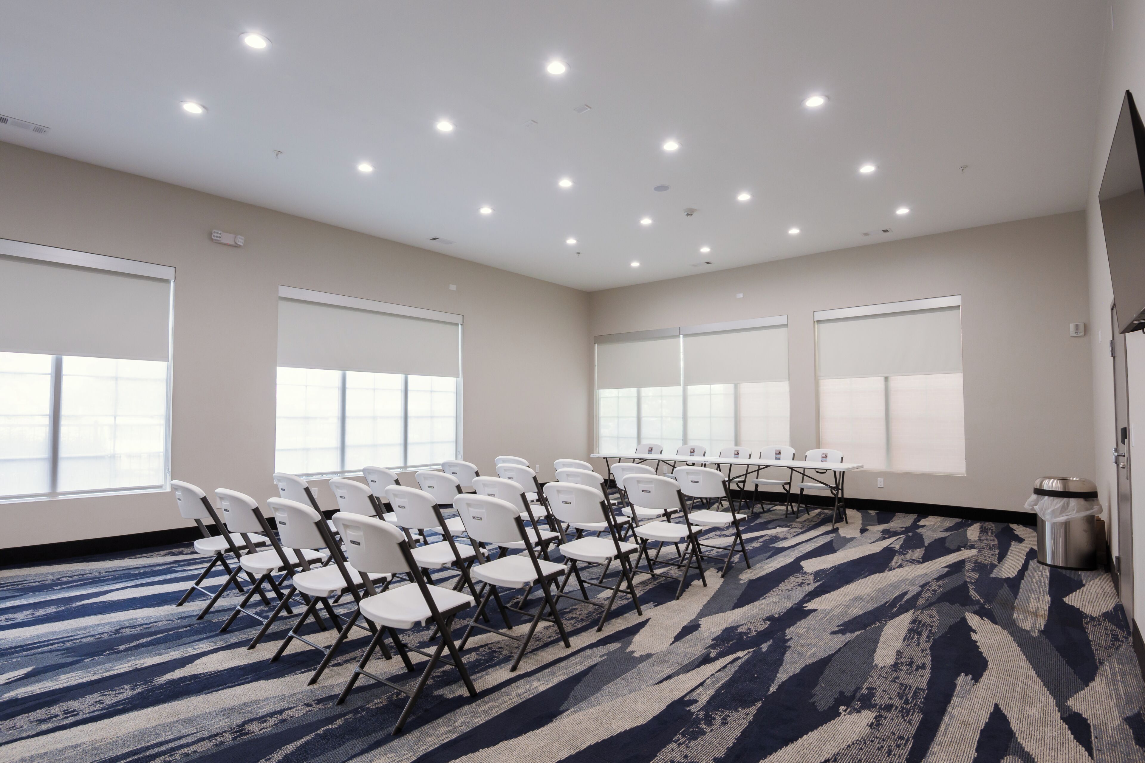 Una sala conferenze con sedie bianche disposte attorno a un lungo tavolo, ampie finestre e una tappezzeria decorata.