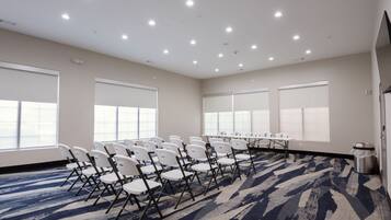 A conference room with white chairs arranged around a long table, large windows, and a patterned carpet.