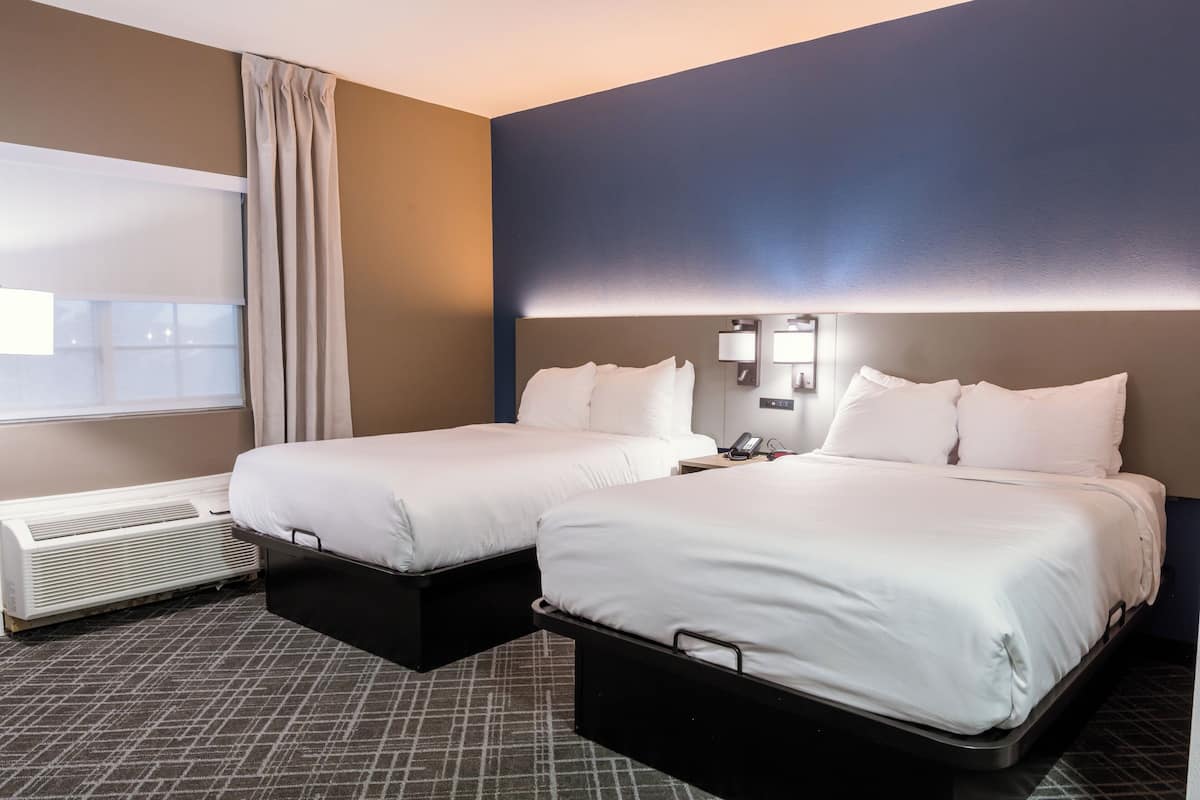 A hotel room with two beds, a window with curtains, a wall-mounted phone, and a heater.