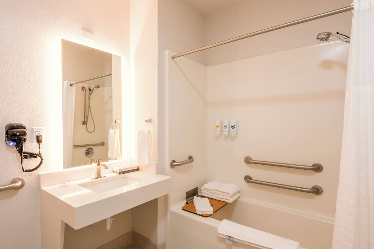 A bathroom with a sink, mirror, towel rack, shower, and hand dryer.