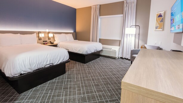 Ein Hotelzimmer mit zwei Betten, einem Schreibtisch, einem Sessel, einem Fernseher und einem Fenster mit Vorhängen.