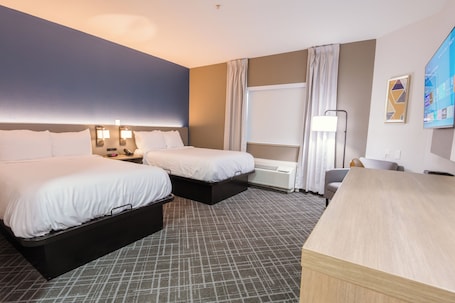 A hotel room with two beds, a desk, a chair, a TV, and a window with curtains.