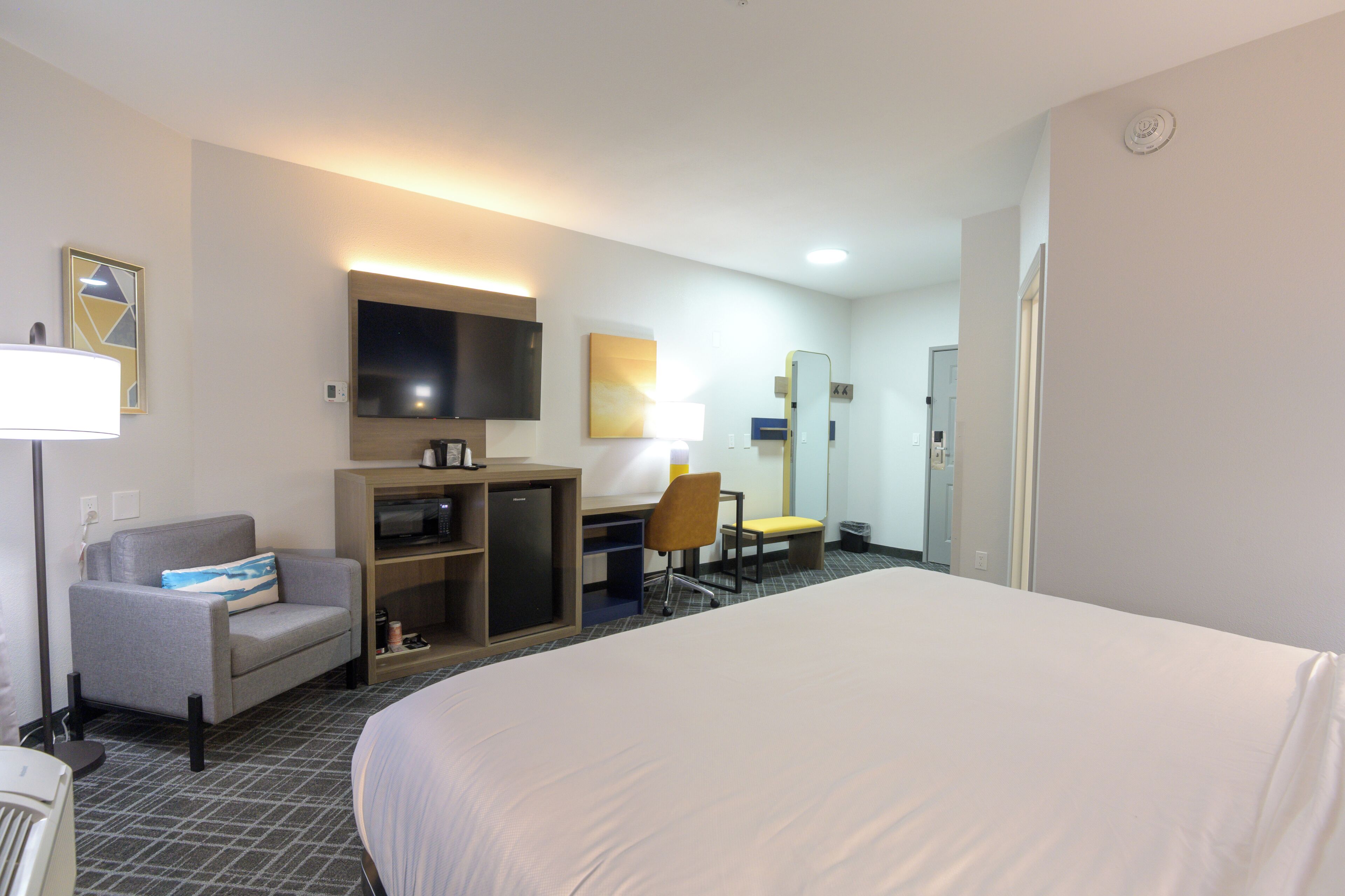A hotel room with a large bed, a desk with a chair, a TV, and a small seating area.