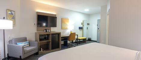 A hotel room with a large bed, a desk with a chair, a TV, and a small seating area.