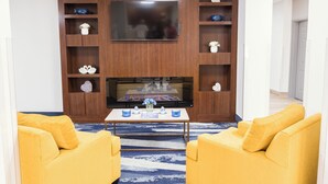 Ein Wohnzimmer mit Flachbildfernseher, Holzregalen mit Dekoration, einem Couchtisch und zwei gelben Sofas.