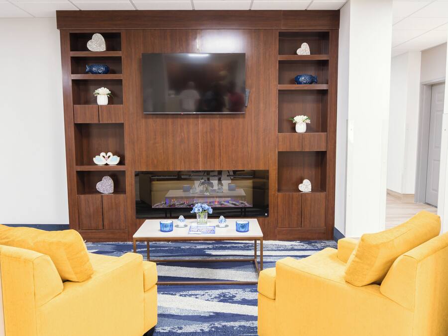 A living room with a flat-screen TV, wooden shelving with decorative items, a coffee table, and two yellow sofas.