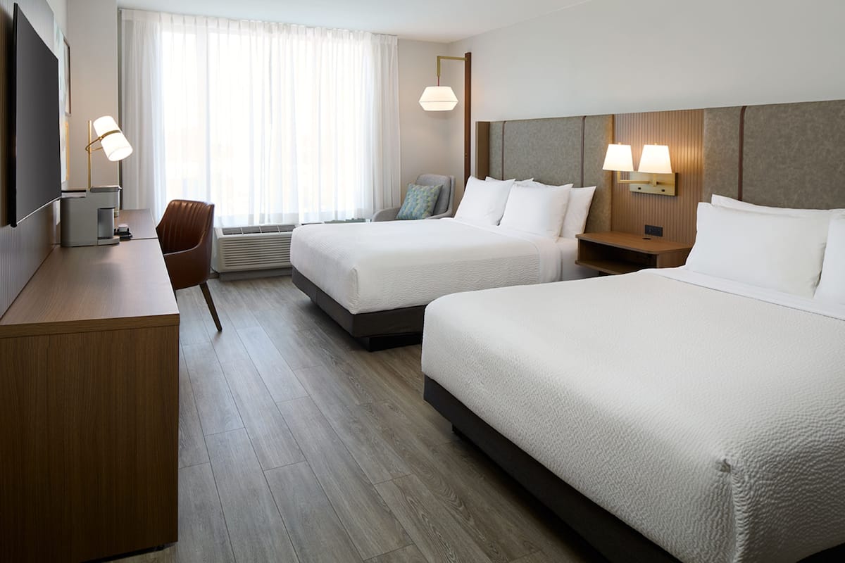 Una habitación de hotel con dos camas, un escritorio, una silla y un televisor.