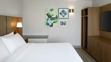 A hotel room with a bed, a desk, a lamp, a TV, and artwork on the wall.