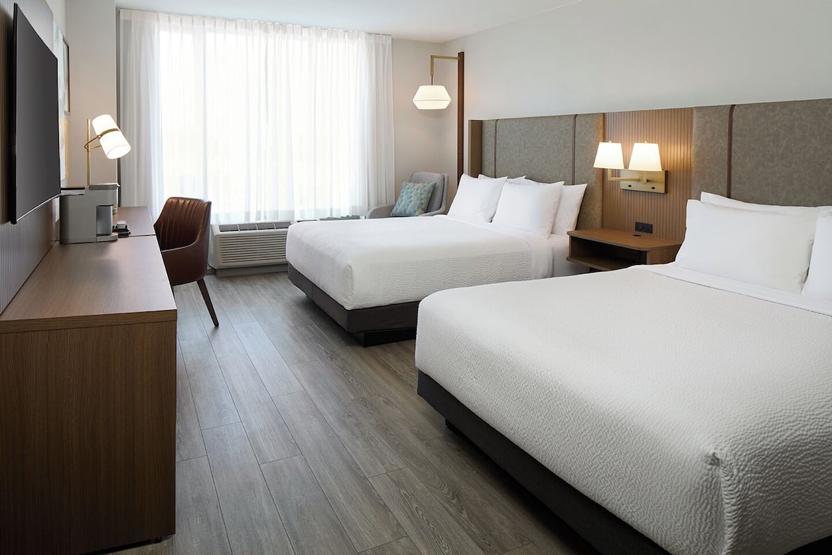 Habitación de hotel con dos camas, un escritorio, una silla y un televisor.