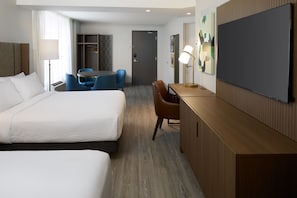 Une chambre d’hôtel avec deux lits, un bureau, une chaise, une télévision et une armoire.