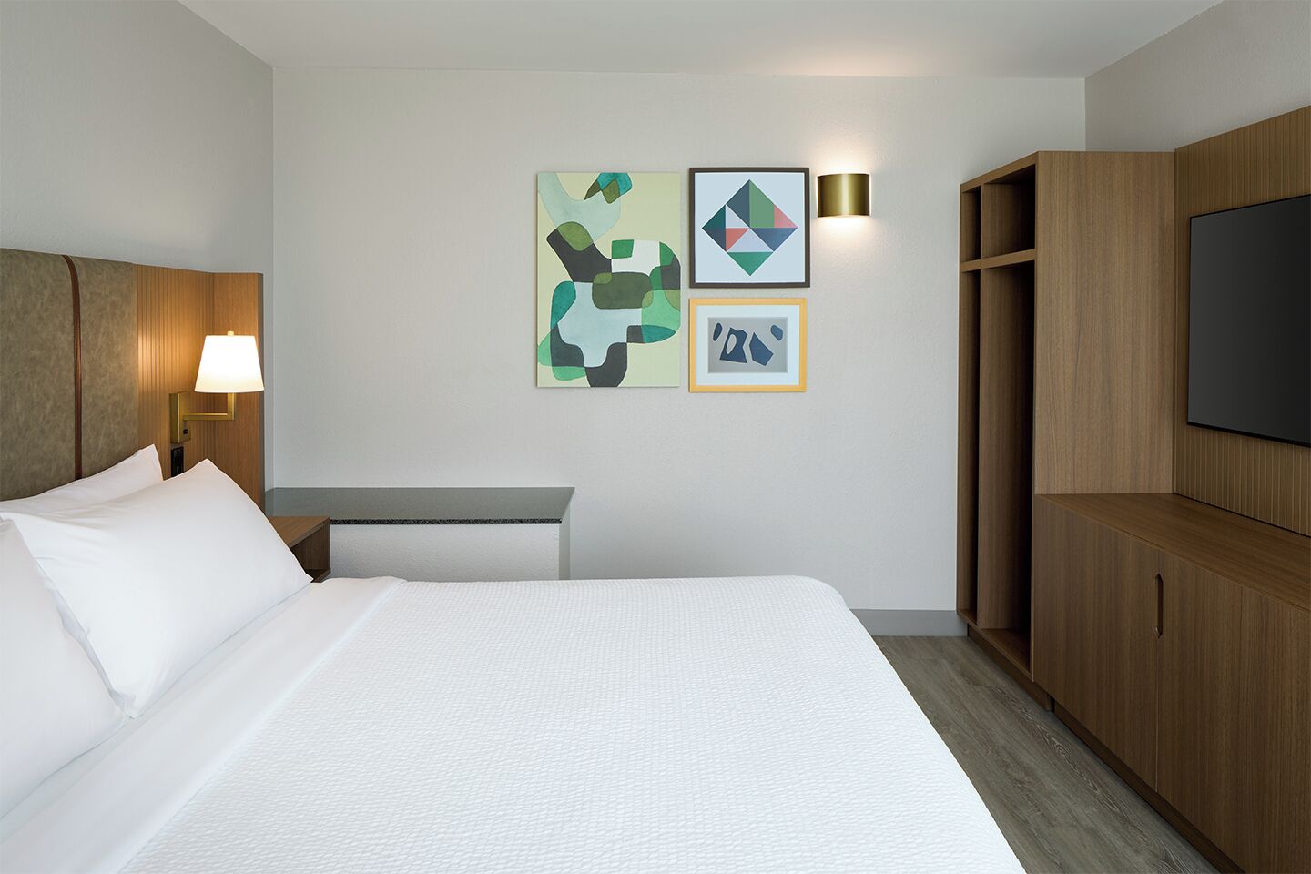 Una habitación de hotel con una cama, un escritorio, una lámpara, un televisor y obras de arte en la pared.