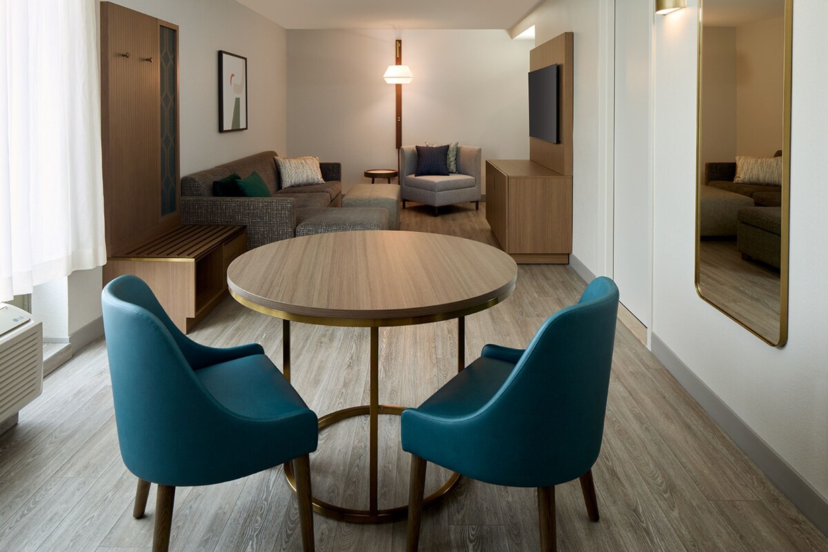 A modern living room with a round wooden table, two blue chairs, a sofa, and a small side table.