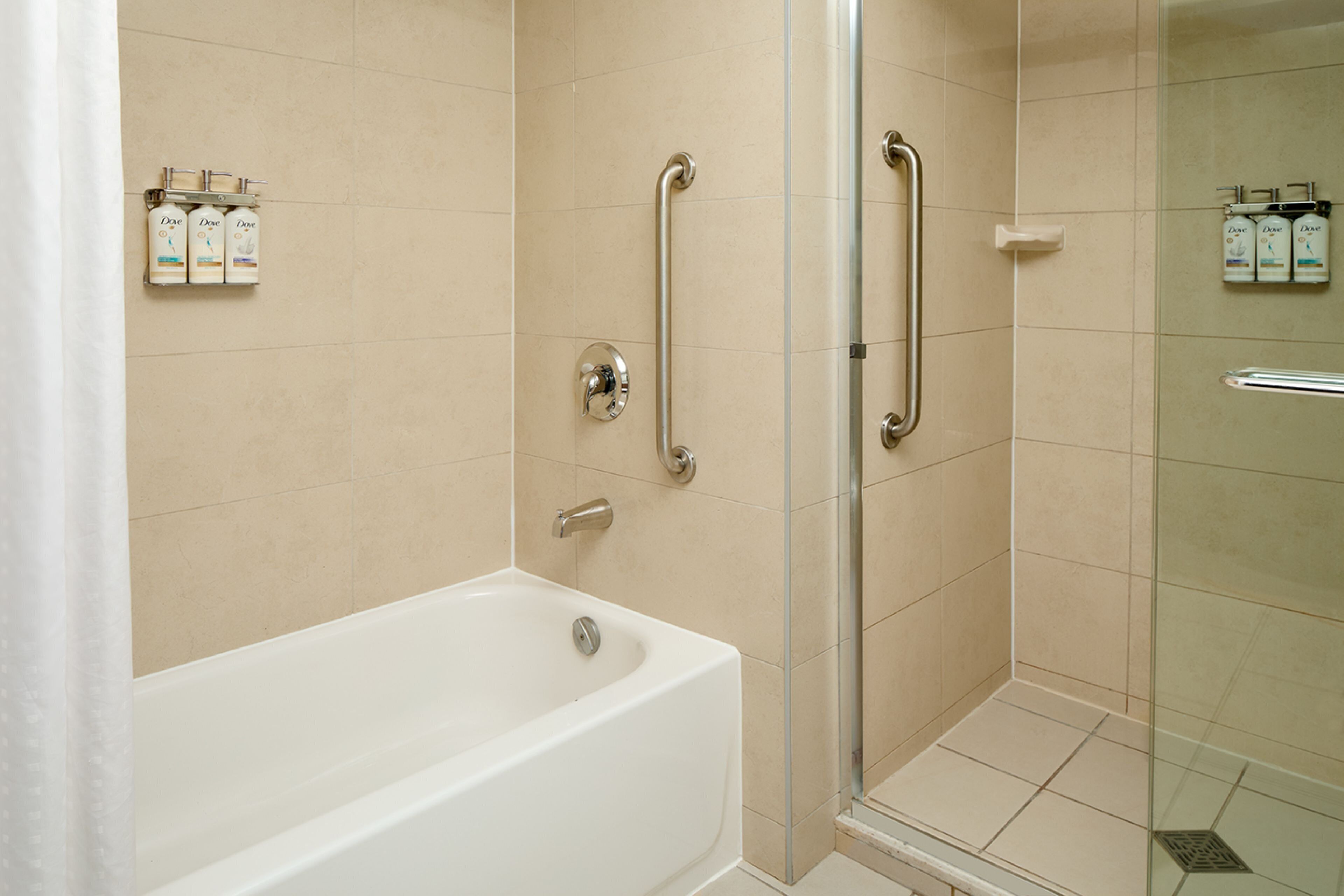 A modern bathroom with a bathtub, a glass shower enclosure, and handrails.