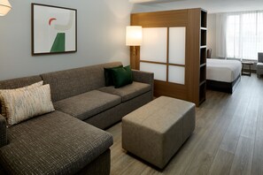 A hotel room with a sofa, ottoman, a bed, a nightstand, a lamp, and a window with curtains. - Holiday Inn & Suites Montreal Airport by IHG (Montreal)