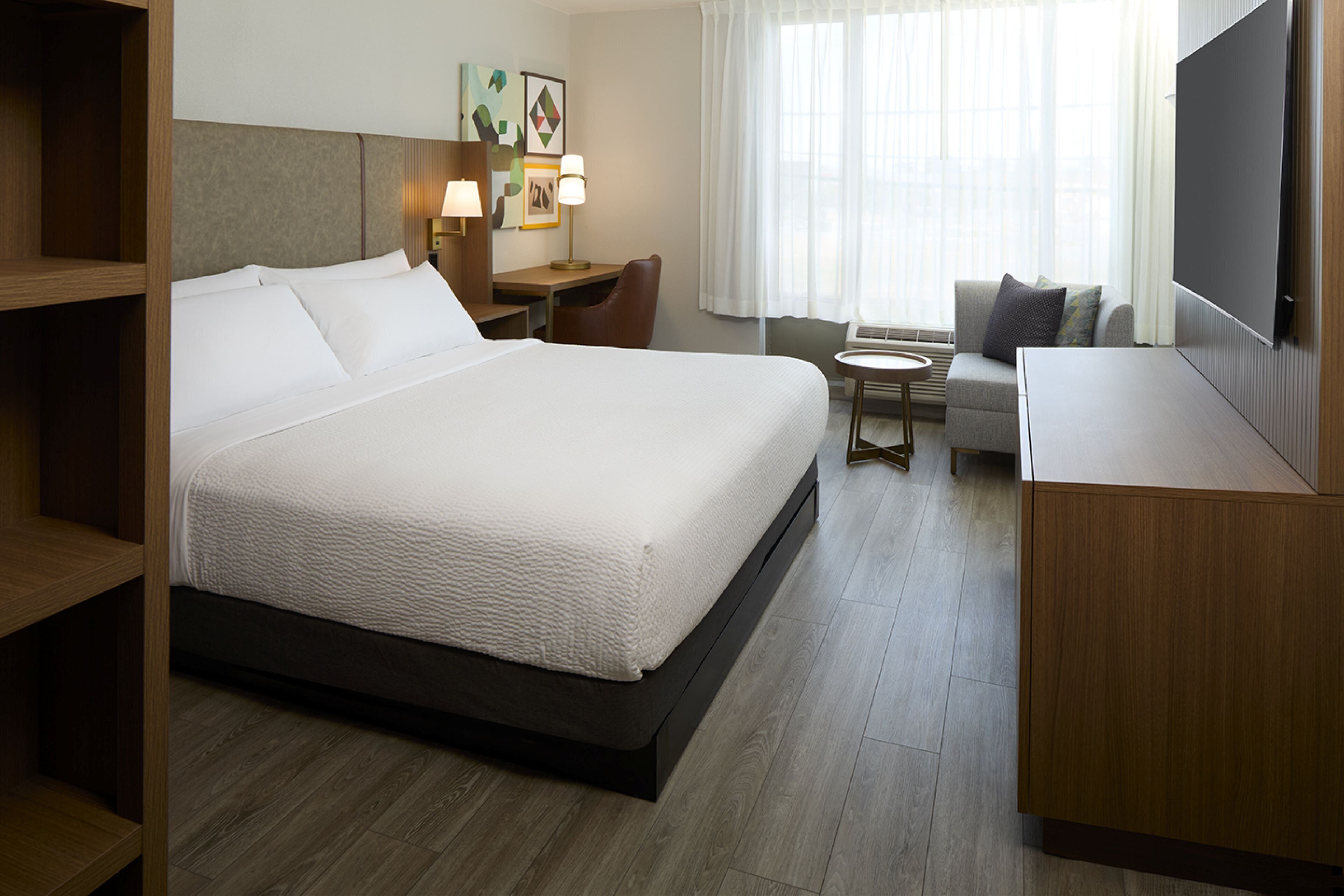 A hotel room with a large bed, a desk, a chair, a sofa, and a TV.
