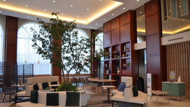 Eine moderne Lobby mit einer gebogenen weißen Couch, einem großen Baum und einem Bücherregal.