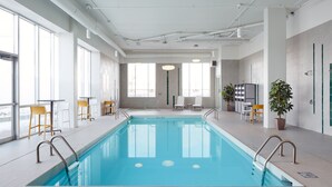 Ein großer, überdachter Pool mit klarem, blauem Wasser, umgeben von weiß gefliesten Wänden und Böden, mit mehreren Stühlen und Tischen am Rand.