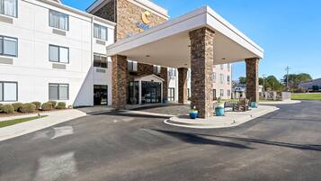 A hotel entrance with a covered walkway, a stone facade, and a clear sky.