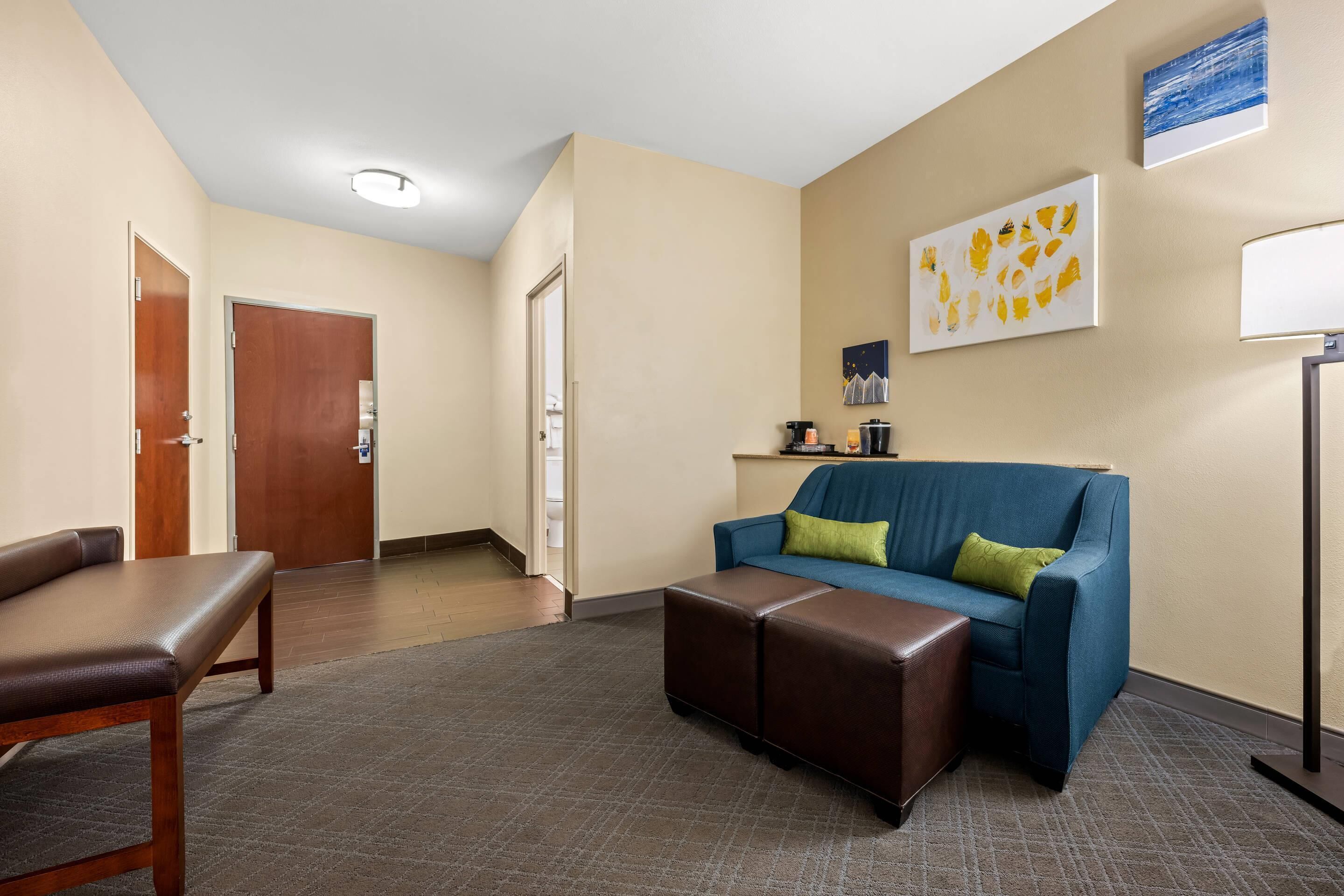 A hotel lobby with a brown leather bench, a blue sofa with green cushions, and a brown ottoman.