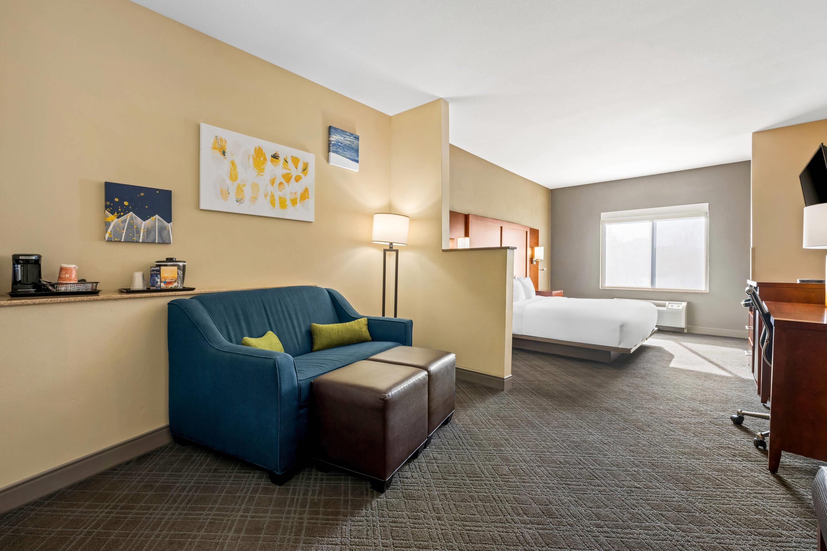 Een hotelkamer met een blauwe bank, een bed, een bureau en kunst aan de muren.