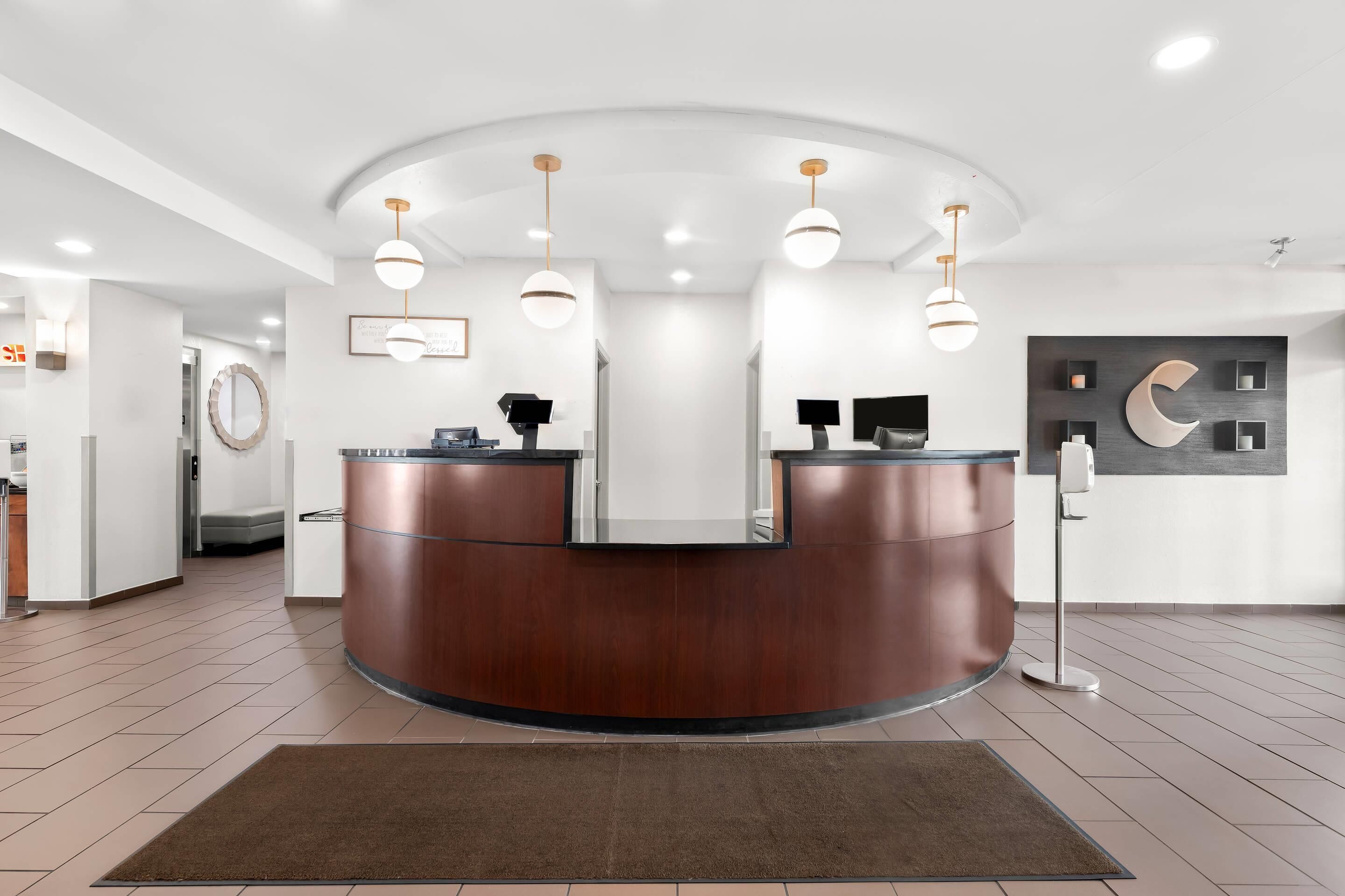 A reception area with a curved wooden desk, a round mirror, and a modern light fixture.
