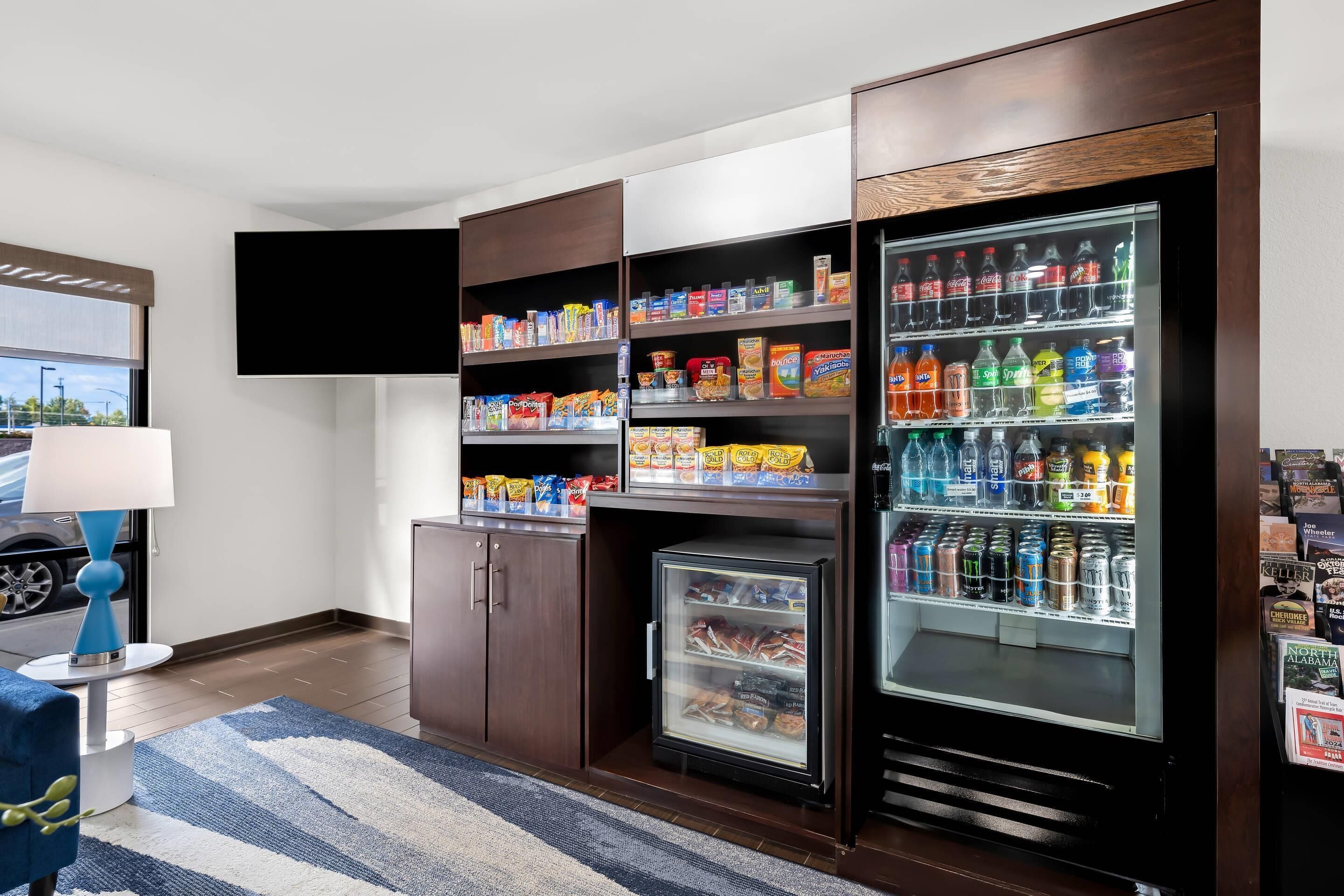Habitación de hotel con minibar, refrigerador lleno de bebidas y un televisor de pantalla plana montado en la pared.