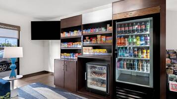 Habitación de hotel con minibar, refrigerador lleno de bebidas y un televisor de pantalla plana montado en la pared.