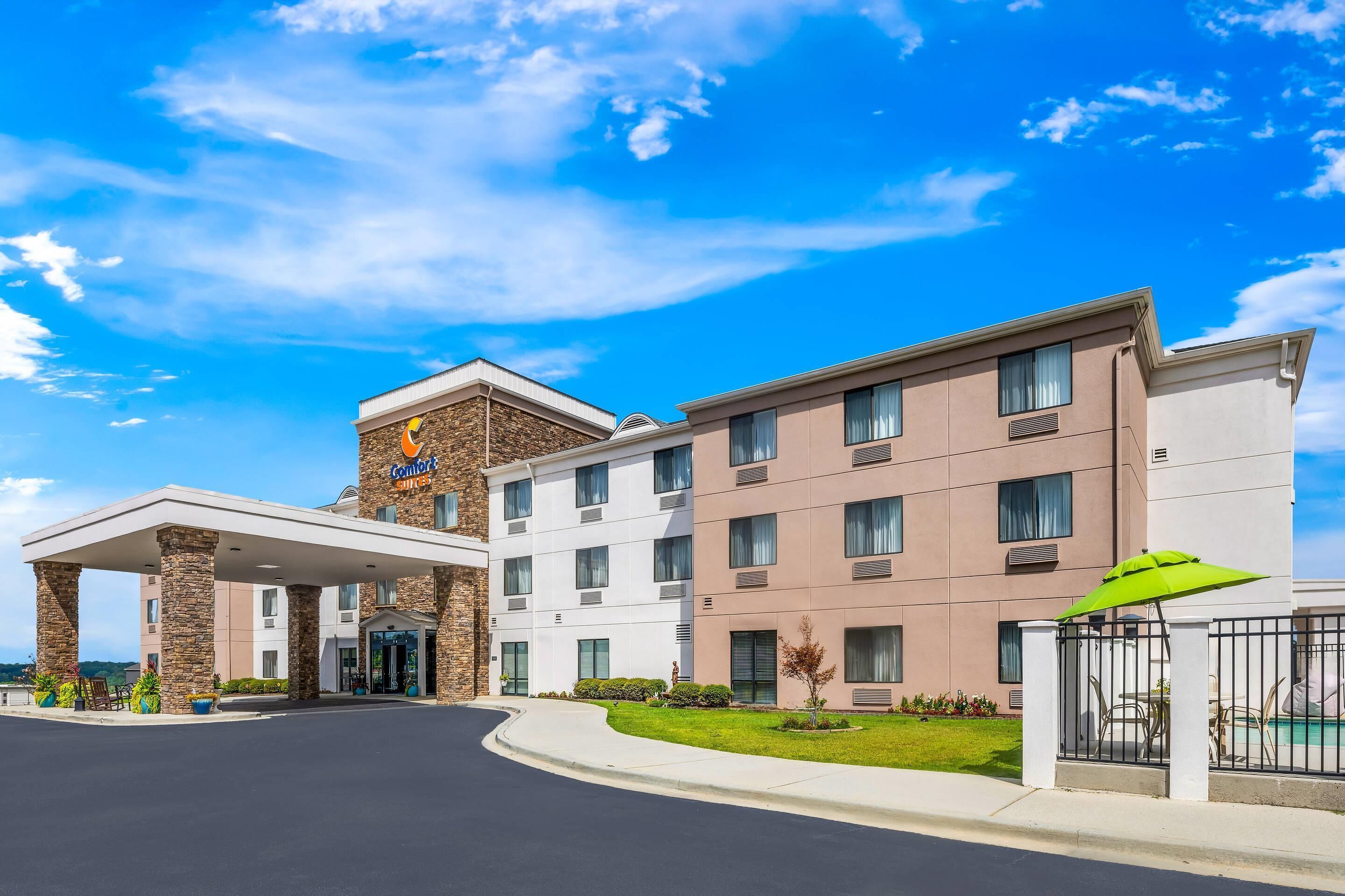 Um hotel com entrada central, vários andares e área de estacionamento.