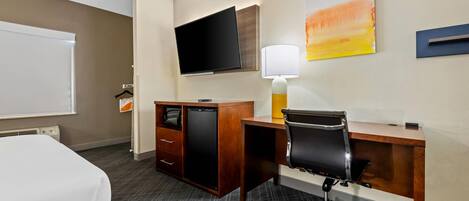 A hotel room with a bed, a desk with a chair, a television, a lamp, and a small cabinet.