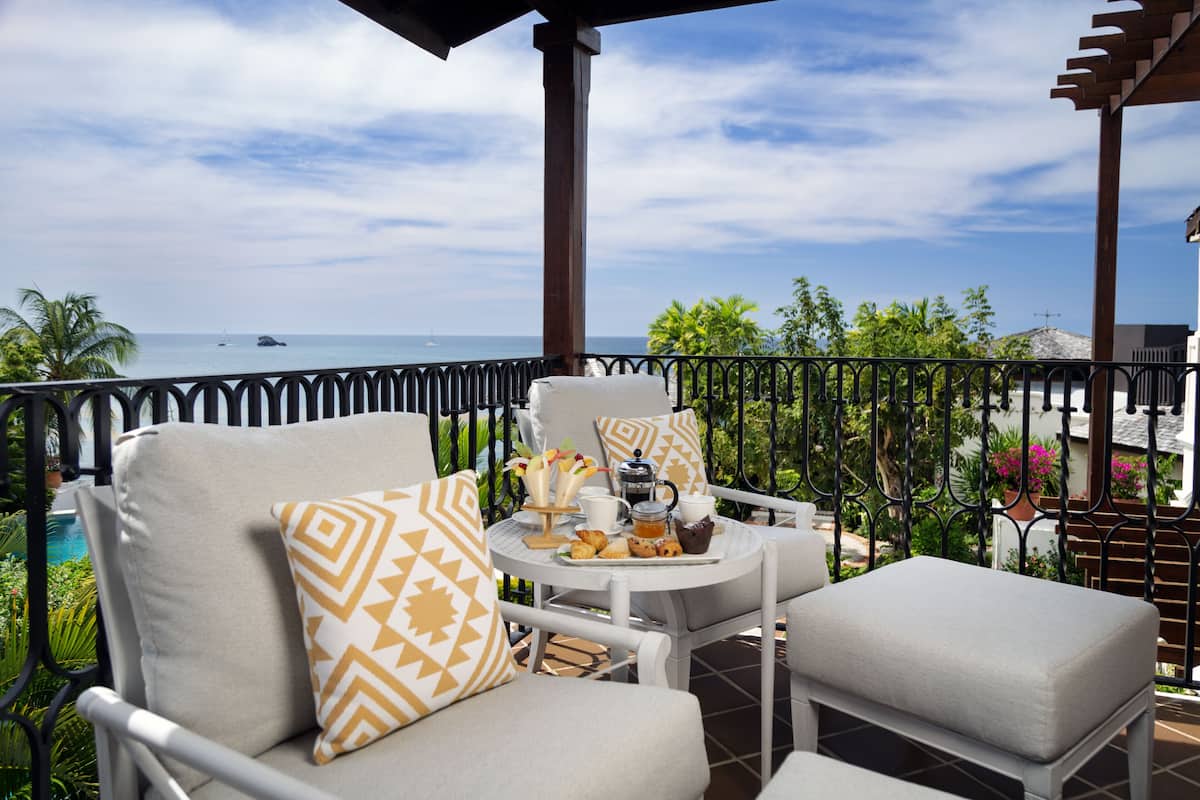 A balcony with a view of the ocean, featuring outdoor furniture and a table with breakfast items.