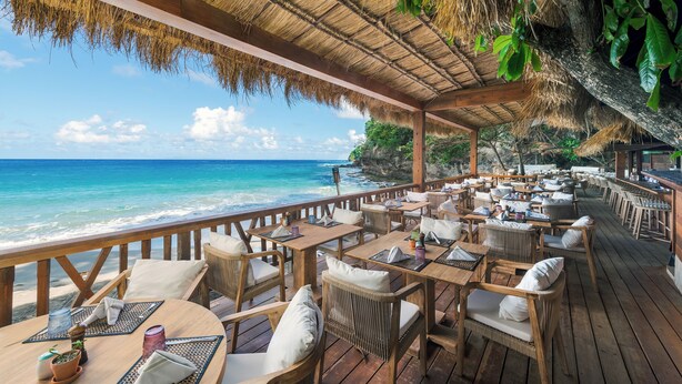 A beachside restaurant with wooden tables and chairs, thatched roof, and ocean views. - Cap Maison Resort & Spa (Gros Islet)