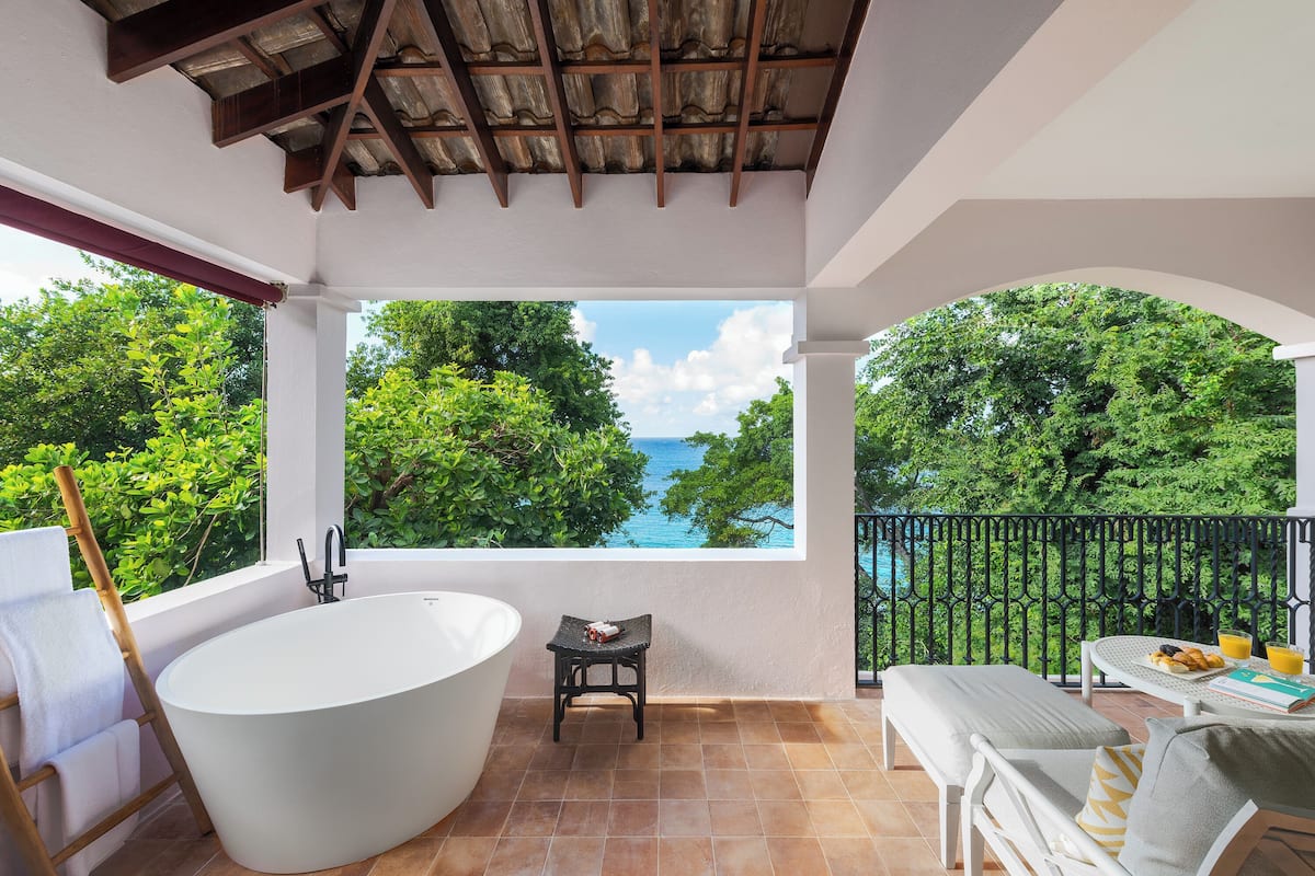 A bathroom with a bathtub, a small stool, and a view of the sea through a large window.