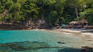 A beach with clear turquoise water, a thatched-roof hut, and a rocky shoreline. - Cap Maison Resort & Spa (Gros Islet)