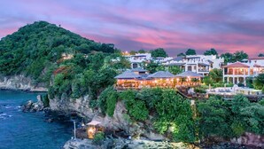 A coastal resort with multiple buildings, some with outdoor seating areas, situated on a cliff overlooking the sea. - Cap Maison Resort & Spa (Gros Islet)