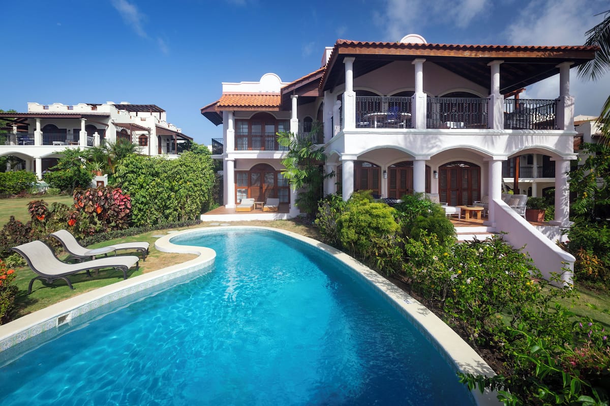 A large, two-story house with a swimming pool, surrounded by lush greenery and a well-maintained garden.