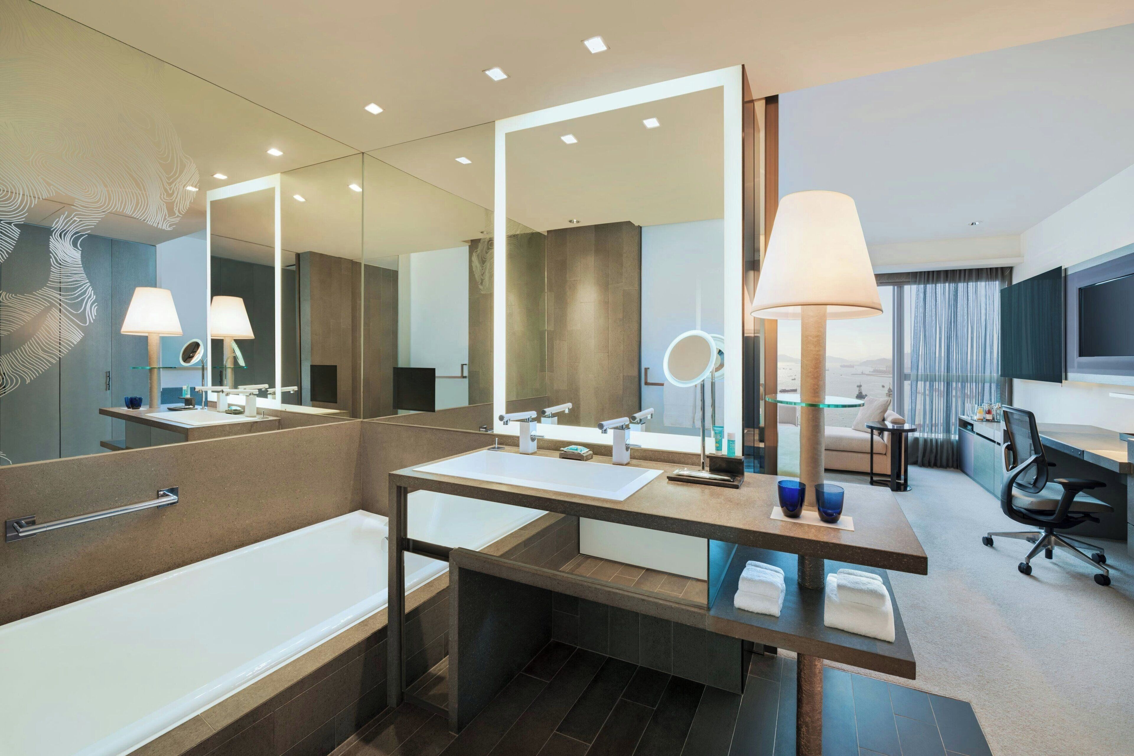 Un baño moderno con bañera, dos lavamanos, un espejo grande y un mueble de tocador con lámpara.