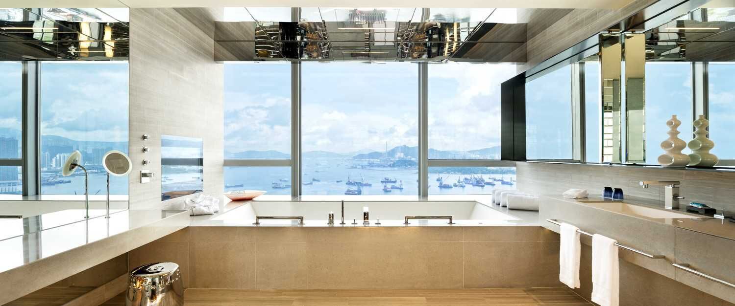 Un baño moderno con una bañera grande, un tocador con espejo y vistas a la ciudad a través de amplios ventanales.