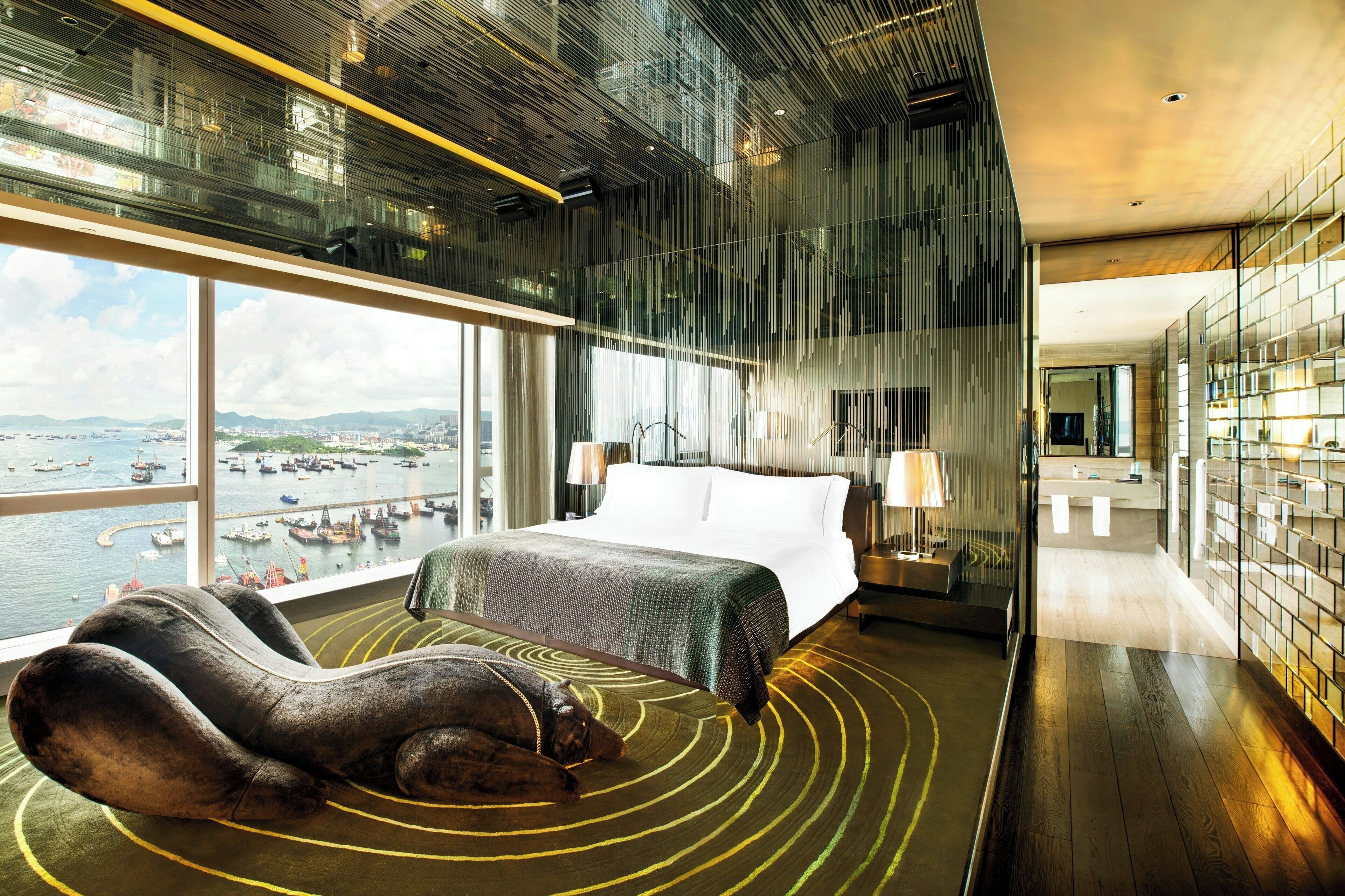 A modern hotel room with a large bed, a view of the harbor, and a unique circular rug.