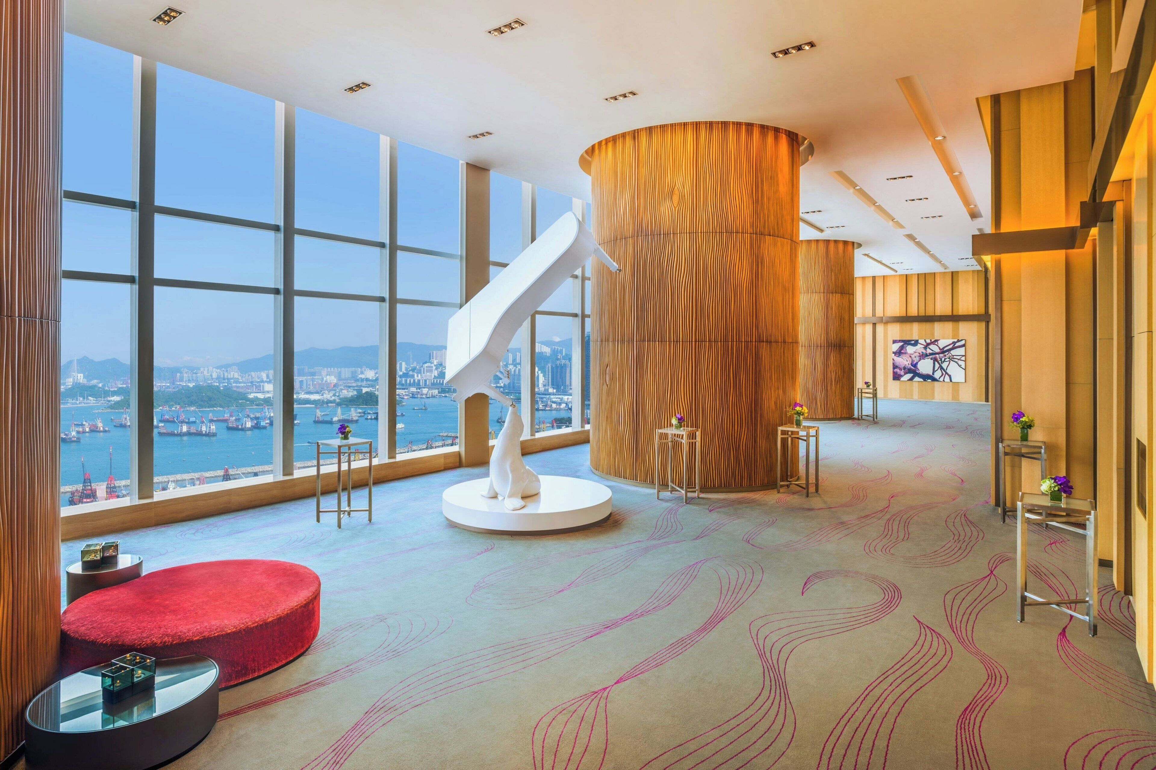 A spacious lobby with large windows, a central wooden column, and a modern staircase.