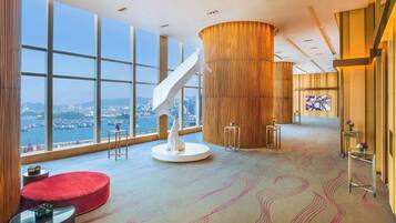 A spacious lobby with large windows, a central wooden column, and a modern staircase.