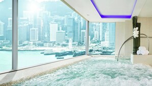 Une salle de spa avec vue sur la ville, un jacuzzi et des serviettes rangées sur une étagère.