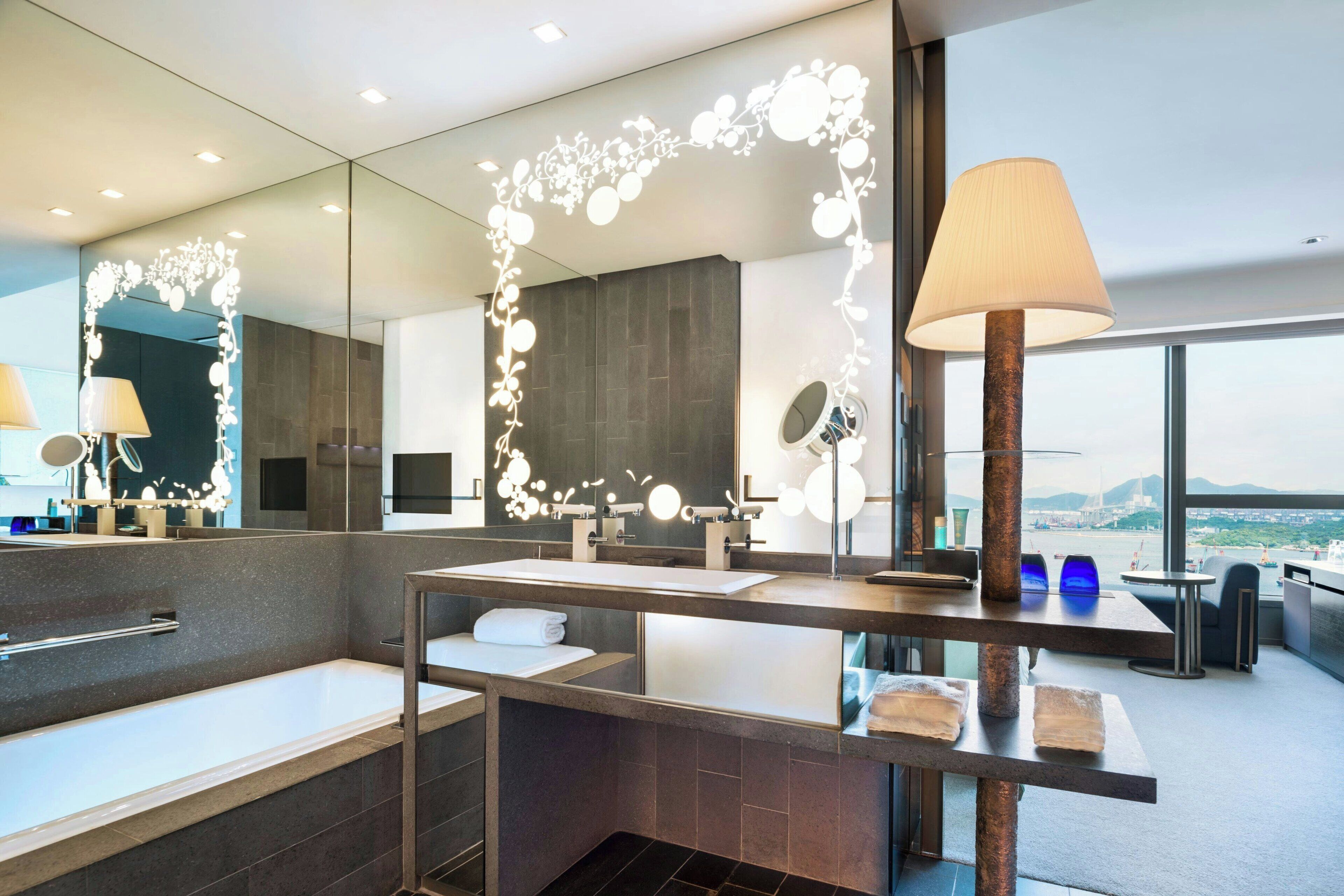A modern bathroom with a large mirror, a bathtub, and a vanity with a towel rack.