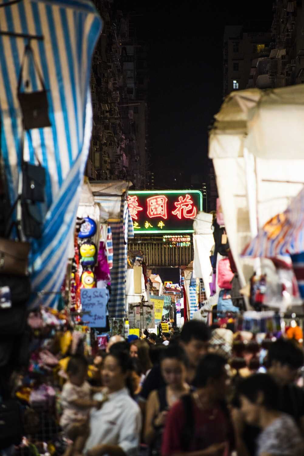 Un mercado callejero concurrido de noche, con letreros de neón y varios puestos.