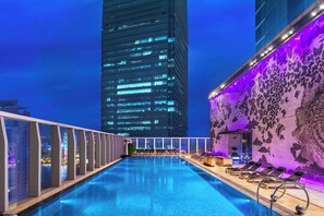 Una piscina al terrat amb vistes a un edifici alt, cadiretes de relax i una paret decorativa.