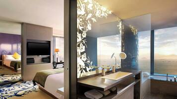 A modern hotel room with a large bed, a TV, a bathroom with a large mirror, and a view of the sea.