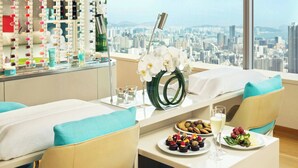 Une chambre d’hôtel avec vue sur la ville, un minibar, une table avec de la nourriture et des boissons, et une grande fenêtre.