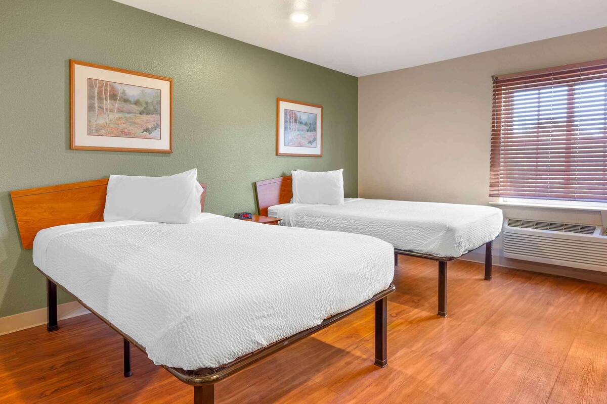 Habitación de hotel con dos camas, cabeceros de madera, paredes verdes y cuadros enmarcados.