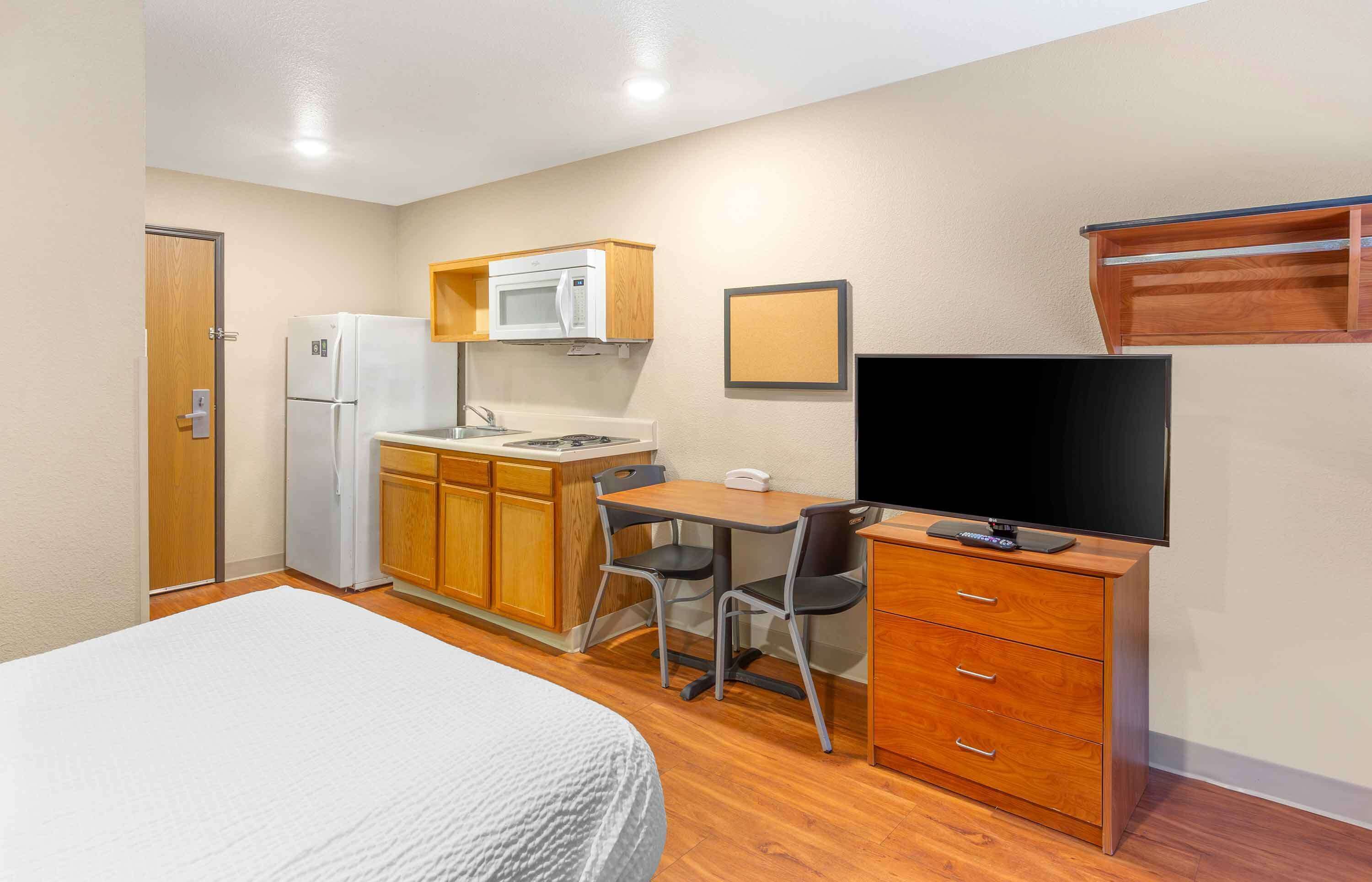 A compact room with a bed, kitchenette, and a TV.